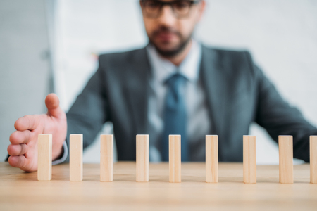 Close-up shot of businessman assembling wooden blocks in row on worktable, dominoes effect conceptの写真素材