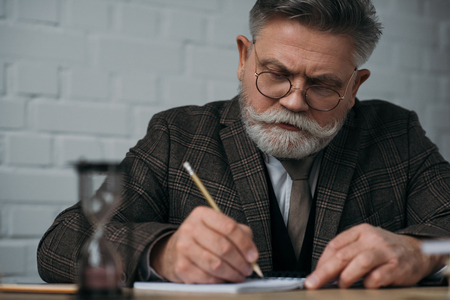 Serious senior man writing in notebook with pencilの写真素材