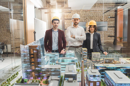 Team of architects in hard hats in front of miniature town model at officeの写真素材