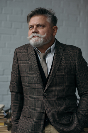 Senior man in stylish tweed suit looking away in front of white brick wall backgroundの写真素材