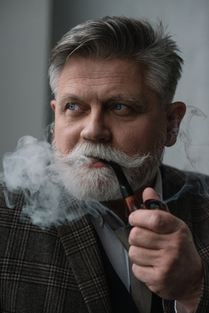 Close-up portrait of handsome senior man smoking pipeの写真素材