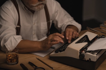 Cropped shot of senior writer working with typewriter isolated on black backgroundの写真素材