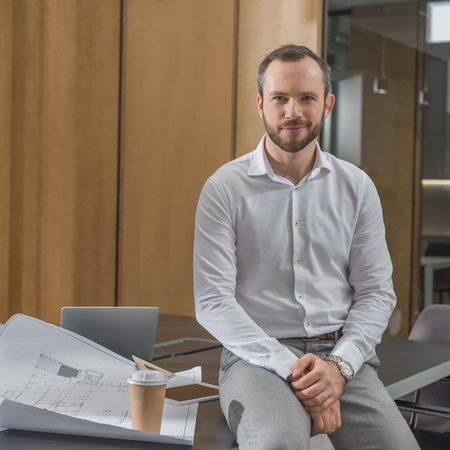 Handsome architect sitting on table with plans at officeの写真素材