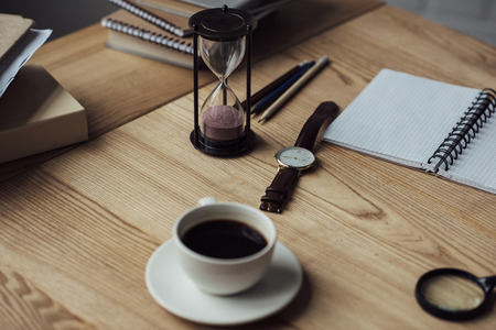 Cup of coffee white hourglass and watch on workplaceの写真素材