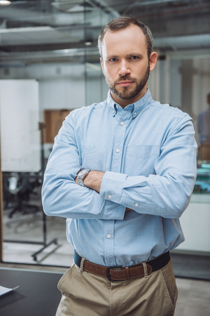 Handsome successful businessman with crossed arms at officeの写真素材