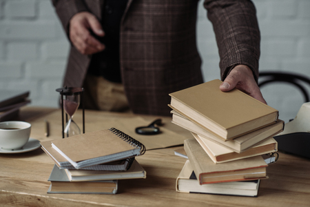 cropped shot of man taking stack of books from tableの写真素材