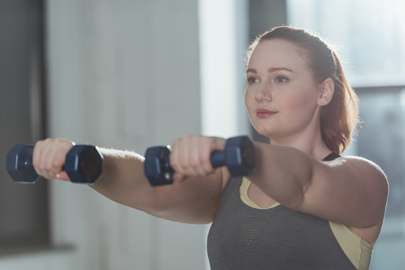 Curvy girl training with dumbbells in gym