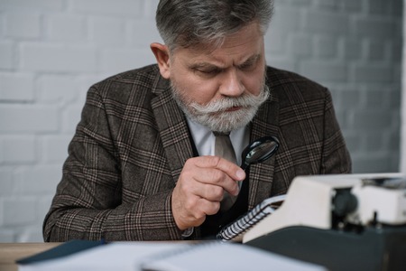 Bearded senior writer reading manuscript with magnifying glassの写真素材