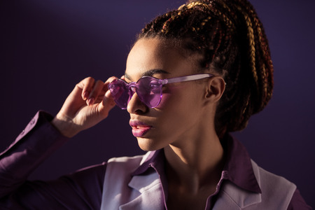 Stylish African American girl posing in purple sunglasses, isolated on purple backgroundの写真素材