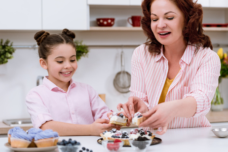 Grandmother and little granddaughter eating delicious tart with berries at kitchenの写真素材
