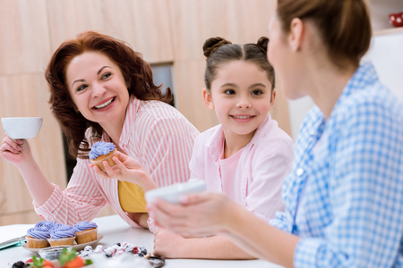 Three generations of women spending time together on kitchen and eating desserts with tea at kitchenの写真素材