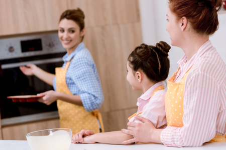 Three generations of beautiful women in aprons baking pastry together at kitchenの写真素材