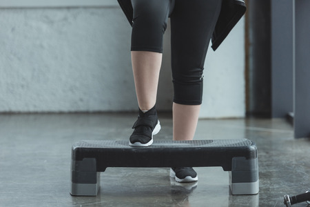 Curvy girl exercising on step platform in gym