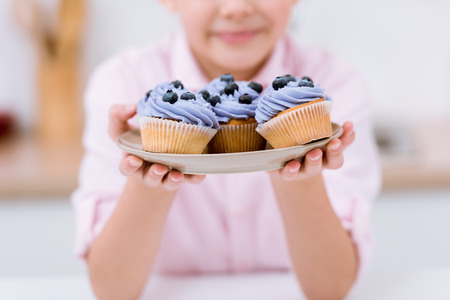 Cropped shot of little child holding plate with blueberry cupcakesの写真素材