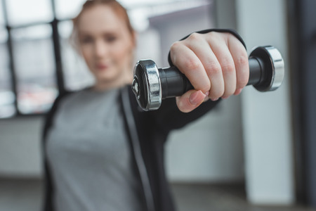 Close-up view of curvy girl lifting dumbbell in gym