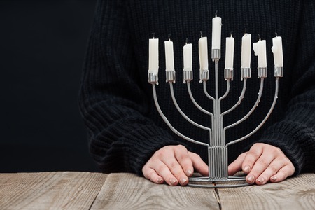 cropped shot of woman standing at wooden tabletop with menorah and candles on black background, hannukah celebration conceptの写真素材