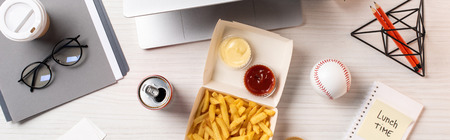 top view of french fries, soda can, baseball ball and office supplies at workplaceの写真素材