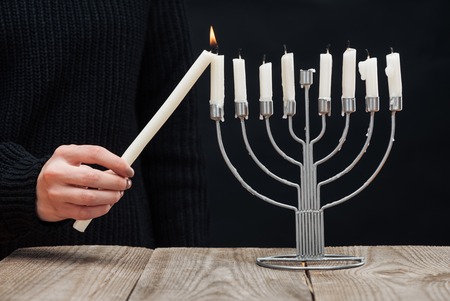 partial view of woman lighting candles on menorah on wooden tabletop on black backdrop, hannukah holiday conceptの写真素材