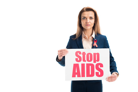 attractive businesswoman with red ribbon on suit showing card with stop aids text isolated on whiteの写真素材