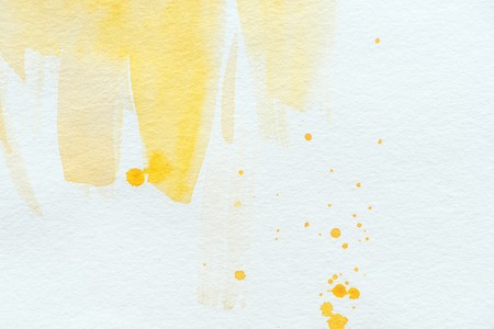 yellow watercolor strokes and splatters on white paper backgroundの写真素材