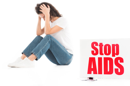 sad woman sitting and touching head isolated on white, stop aids card on foreground
