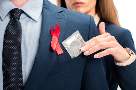 cropped image of businesswoman giving condom to businessman with red ribbon on suit isolated on...