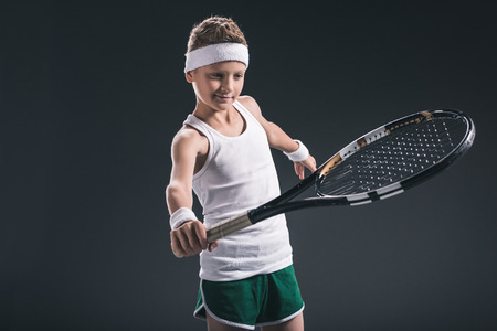 portrait of boy in sportswear with tennis racket on dark backgroundの写真素材