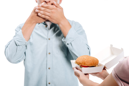 cropped image of man covering mouth, woman proposing burger isolated on whiteの写真素材