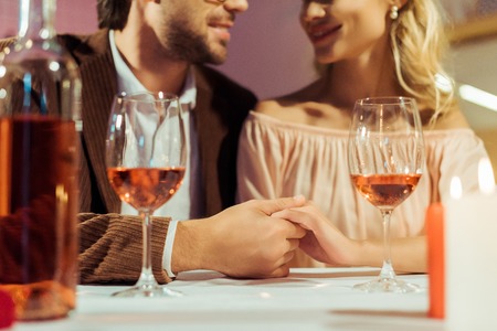 cropped image of couple holding hands and having date at table with wine glasses in restaurantの写真素材