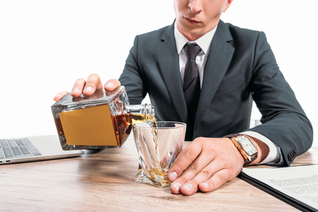 cropped image of businessman pouring whiskey into glass at workspace isolated on whiteの写真素材