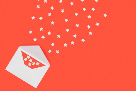 top view of open white envelope with red card and small white stars isolated on red backgroundの写真素材