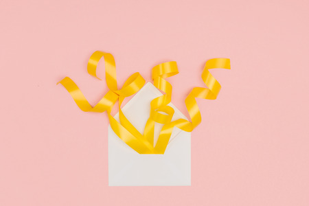 close-up view of open white envelope with yellow ribbons isolated on pink