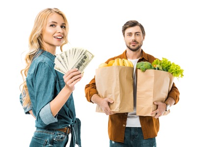 woman showing money while her boyfriend standing behind with products in shopping bags isolated on whiteの写真素材