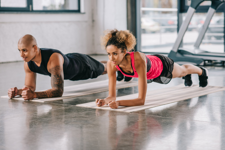 young african american couple of athletes doing plank on fitness mats at gymの写真素材