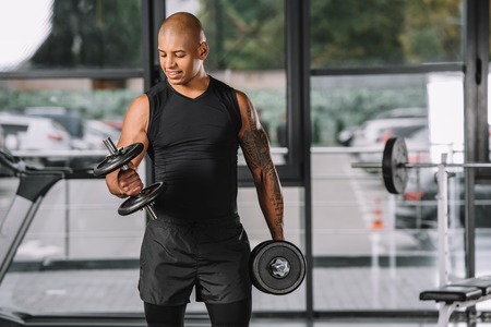 african american male athlete with tattooed hand exercising with dumbbells at gymの写真素材