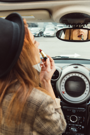 Partial view of woman looking at back mirror and using red lipstick in carの写真素材