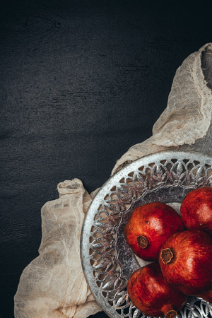 Food composition with ripe and fresh pomegranates, metal bowl and gauze on black tabletopの写真素材