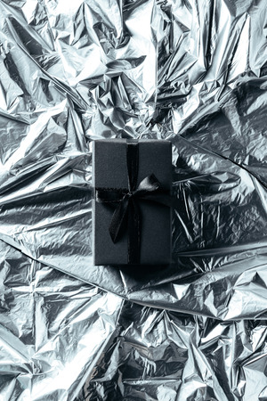 top view of gift box with black ribbon on silver wrapping paper backdropの写真素材