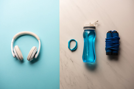 flat lay with headphones, bottle of water, jump rope and fitness tracker on blue and marble