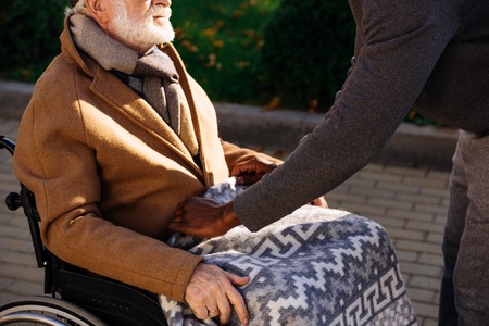 Cropped shot of African american man covering senior disabled man in wheelchair with plaid on streetの写真素材