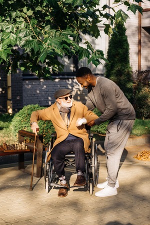 African american man helping senior disabled man to get up from wheelchair on streetの写真素材