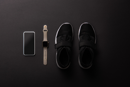 Elevated view of arranged smartphone with blank screen, smartwatch and sneakers isolated on blackの写真素材