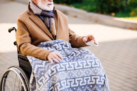 Cropped shot of senior disabled man in wheelchair with plaid on legs on street
