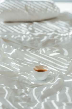Close up view of cup of aromatic coffee on white bed sheetの写真素材