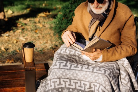 Cropped shot of senior disabled man in wheelchair reading book on streetの写真素材