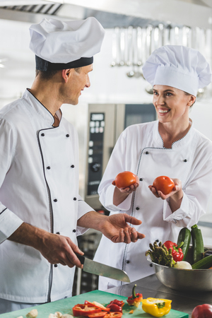 smiling chef showing ripe tomatoes to colleague at restaurant kitchenの写真素材
