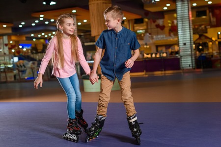 adorable kids holding hands while skating together on roller rinkの写真素材