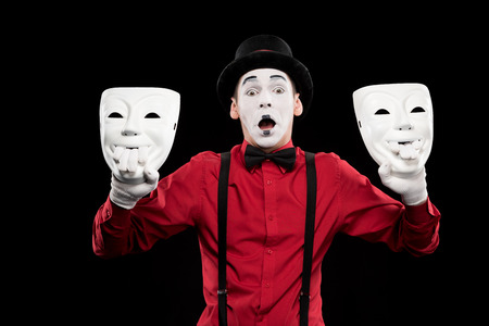 shocked mime holding two masks isolated on blackの写真素材