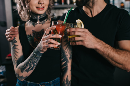 cropped image of bartenders clinking with drinks at bar