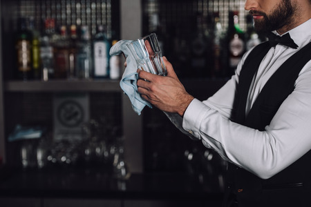 cropped image of bartender cleaning glass with rag in evening